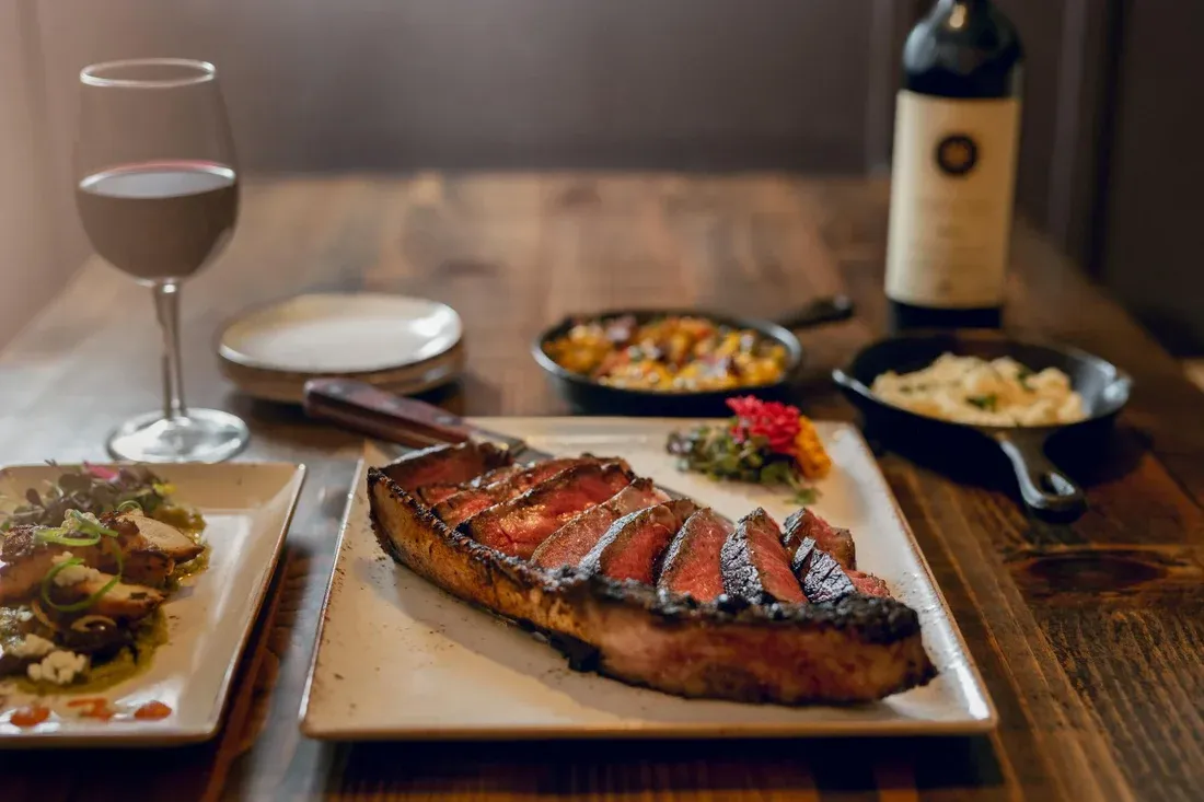 A charred, sliced steak plated with sides and a glass of red wine at Jimmy P's Charred
