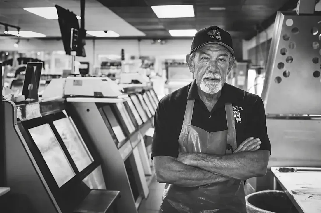 A butcher in a Jimmy P's apron stands with arms crossed inside the shop