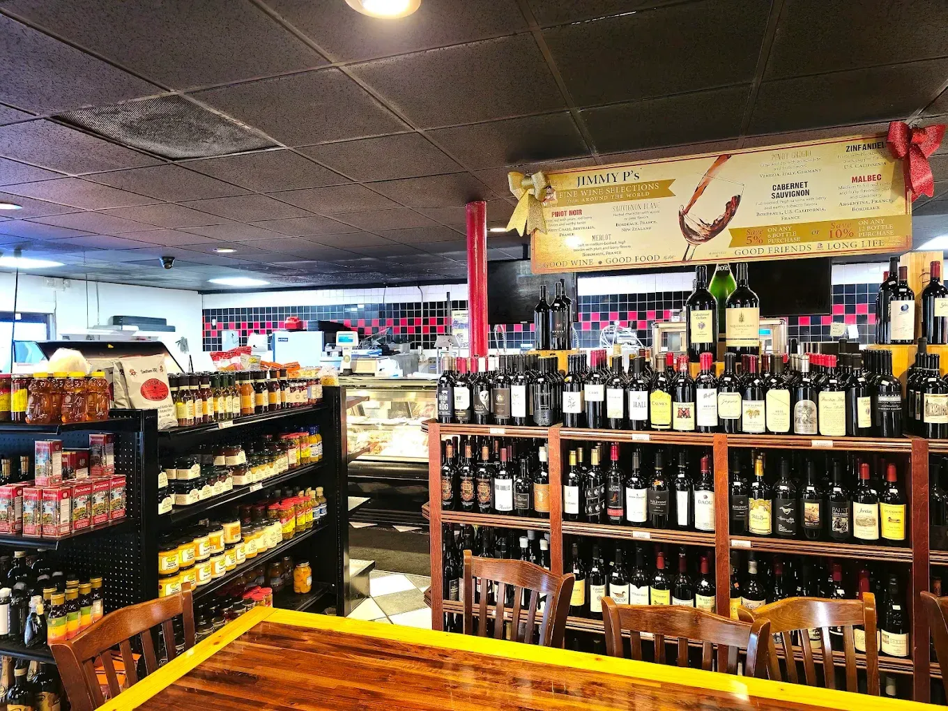 Wine shelves, a deli case, and a wooden table inside the Jimmy P's Naples shop