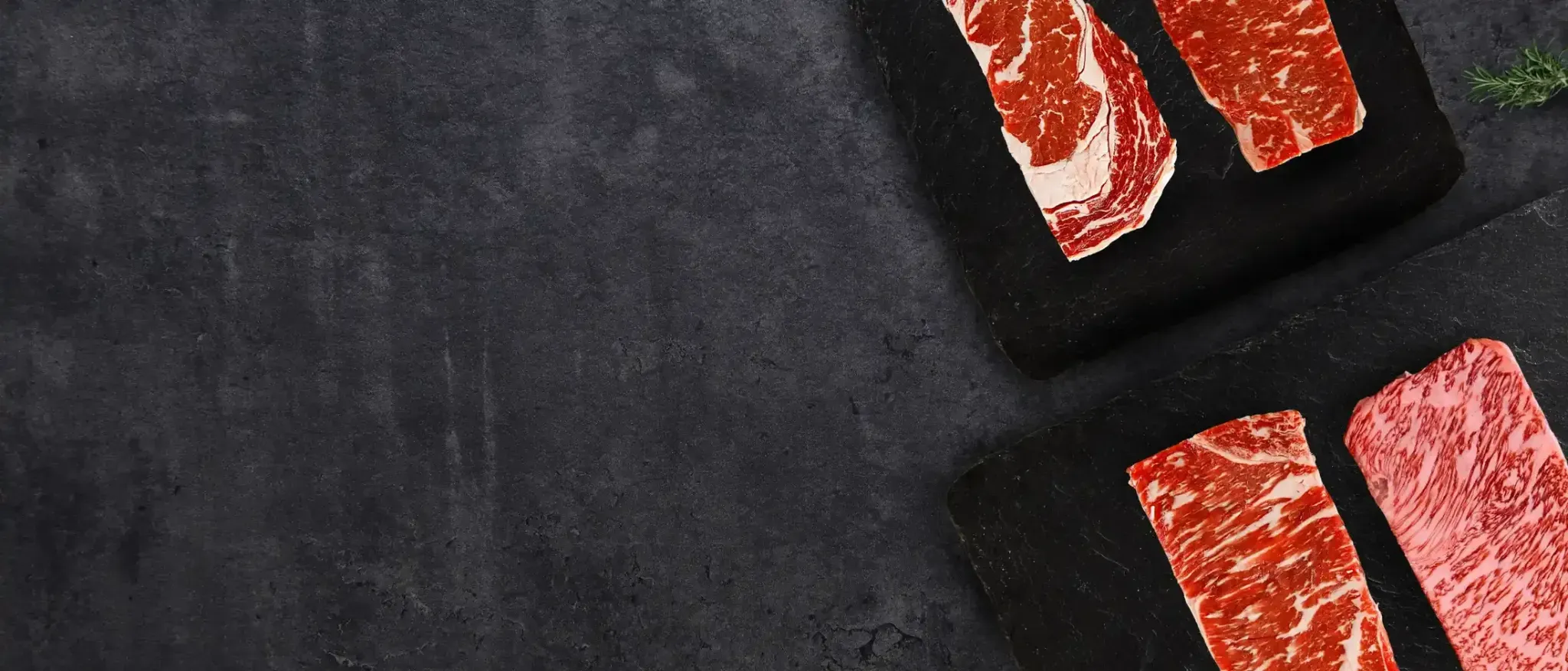 Raw steaks arranged on black boards against a dark surface